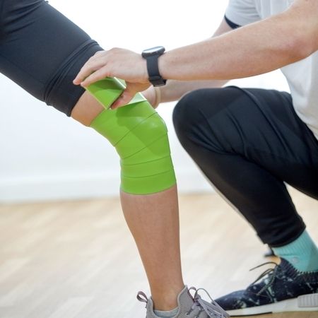 Physiotherapeut bringt elastisches Band am Knie einer Patientin an: Flossing