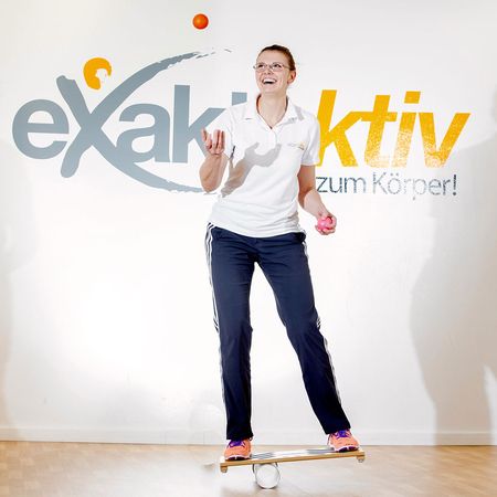 Eine Mitarbeiterin demonstriert eine Gleichgewichtsübung mit Bällen und einem Brett