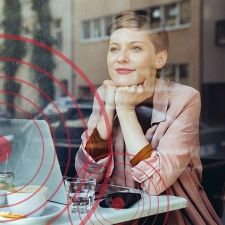Eine Frau sitzt mit verschiedenen Endgeräten an einem Tisch