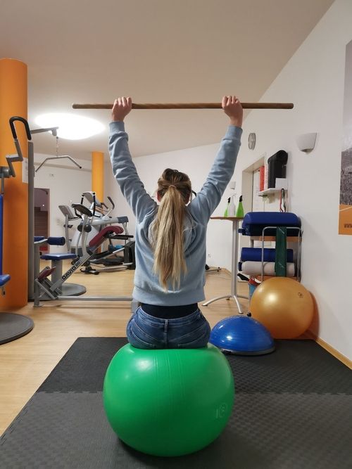 Patientin trainiert ihre Bewegung mit einem Stab und einem Ball