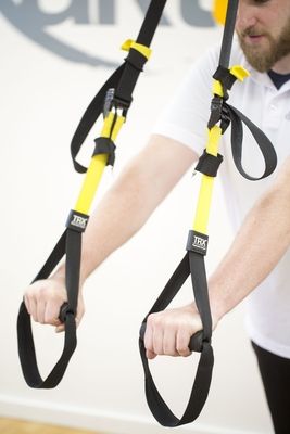 Ein Mitarbeiter demonstriert wie der TRX-Slingtrainer funktioniert