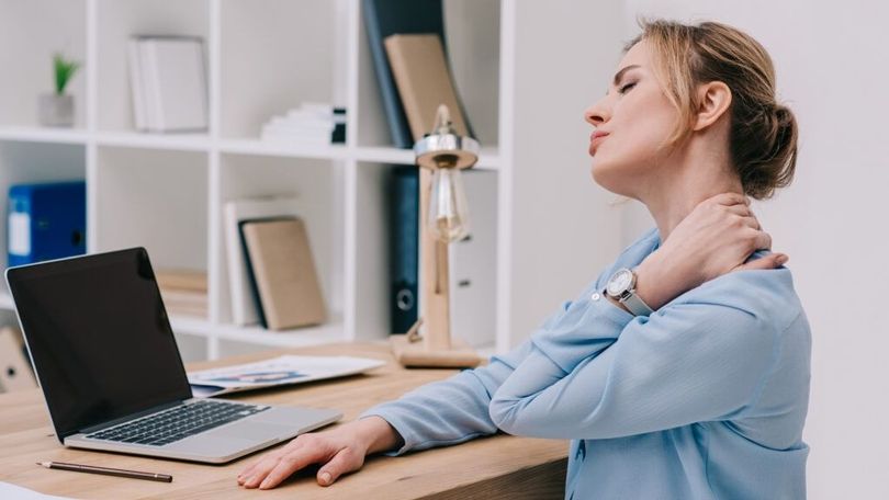 Frau am Computer streckt ihren Nacken